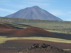 A volcanic cinder cone, with a conical mountain rising in the background