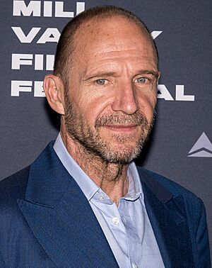 Fiennes in a suit, standing on the red carpet