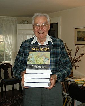 Smiling older man holding a stack of books in front of him; the top one is tilted up so the title, "World History", is visible.