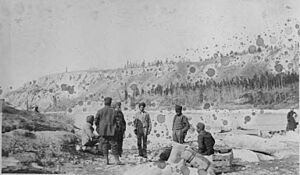 Sikh men in turbans sitting and standing on rocky bank with bags and supplies, Whitehorse, Yukon Territory, April 1906 (AL+CA 7021)