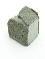 Roughly cube shaped piece of dirty grey metal with an uneven superficial structure. 