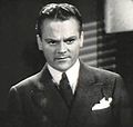 Head and shoulders shot of Cagney, looking stern, wearing a suit with a white handkerchief in his pocket.