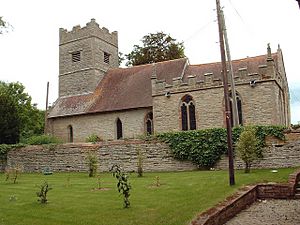 A stone church with red tiled roofs seen from the south.  Extending from the chancel on the right is a battlemented chapel and, to the left, the tower is also battlemented