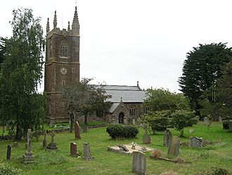 Stone building with square tower. In the foreground are gravestones and trees.