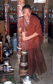 Monk in red robes churning butter tea in a wooden butter churn