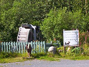 Water wheel and grindstone by side of Seward Highway. The sign reads: "Moose Pass is a peaceful little town, if you have an axe to grind, do it here."