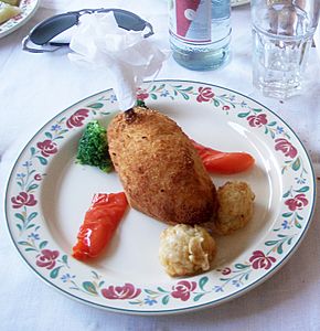A chicken Kiev on a plate garnished with vegetables. A humerus bone is attached and covered with a frilled paper napkin