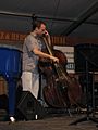A jazz bassist playing double bass using an amplifier and speaker cabinet for a show.
