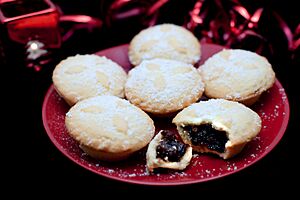 Six mince pies on a plate, sprinkled with sugar and with one broken open