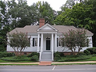 Photo of a one-story home painted white with black shutters and a porch with four pillars.