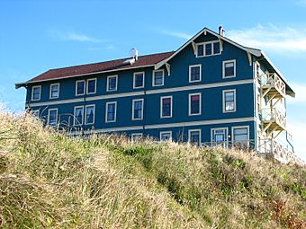 Photograph of the New Cliff House, with three green-painted stories and a peaked roof visible above a grassy bank