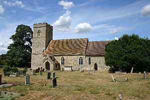 A stone church with red-tiled roofs seen from the south; on the left is an embattled tower, and to the right is the nave with a south porch, and a lower chancel