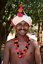 A shirtless man with dark skin wearing a turban with flowers in it