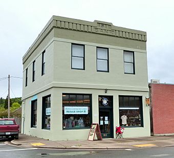 Photograph of a small, two-story commercial building on a city street corner. The cornice inscription reads, "1911 — BANK".