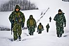 Soldiers in green camouflage gear trudge through snow during a snowstorm