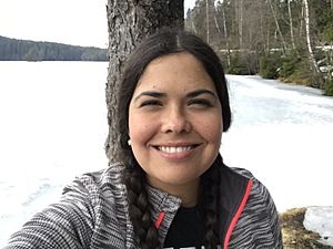 Tara Houska smiling and looking directly at the camera, standing in snow covered woods