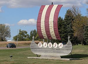 Wooden shape of ship, with fabric sail over it; five painted shields on the side of the ship bear letters spelling out "Wausa"