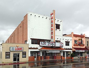 Photograph of frontage and side of white adobe theater building on wet small town Texas street
