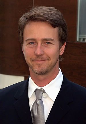 A portrait of Edward Norton, a blonde Caucasian man in a white plaid shirt. He is smiling towards the camera.