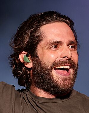 Close-up shot of country music singer Thomas Rhett, wearing a gray shirt and green earpiece