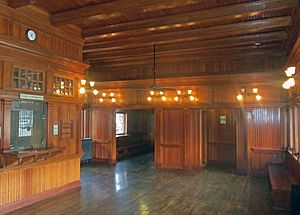 A room paneled in vertical wood planking, with a similar ceiling and floor. Antique lights and a ceiling fan hang from the ceiling.