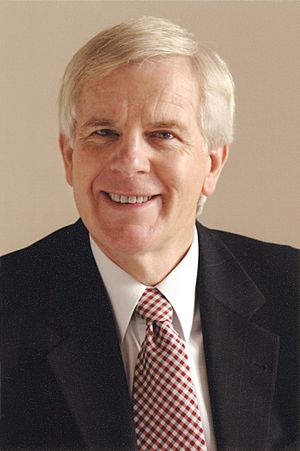 White man in his late sixties, dark jacket, white shirt and tie