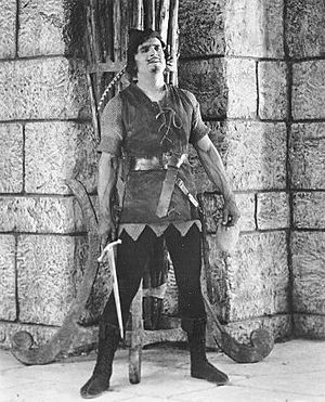 Fairbanks Robin Hood standing by wall w sword