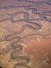 View from an airplane: A river meanders this way and that through a reddish-brown landscape.