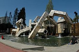 A series of angular, jumbled, concrete pieces, with water running through them, set in a pool.