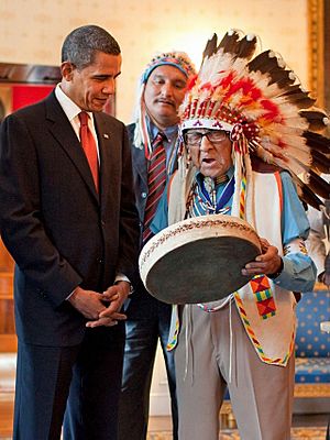 Joe Medicine Crow in full feathered headdress plays a drum for U.S. President Barack Obama