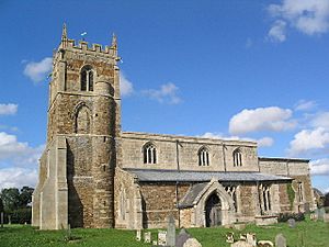 A stone church seen from the south.  On the left is a battlemented tower with a semicircular stair turret, in the middle is the nave with a clerestory and a porch, and to the right at a lower level is the chancel