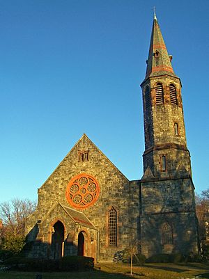 A tall stone building with a pointed roof and a narrow tower rising high from its right.