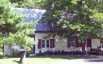 A stone house painted white with green and red trim behind some trees