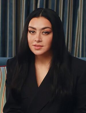 Portrait of Charli XCX, a young woman with long, dark hair wearing a black blazer.