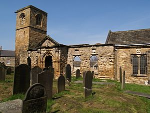 A stone church seen from a slight angle, with a flet-topped tower at the left, then the ruined south wall of the nave, and on the right part of the chancel