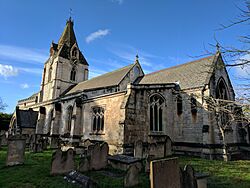 Side view of light coloured stone church with two stepped ranges ending in tower to left against a medium blue sky with white clouds on a sunny day