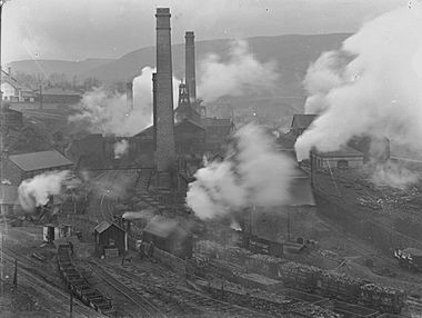 Black and white photograph of a colliery with tall chimney stacks, railway lines and coal wagons