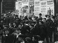 A view of a crowd and some turn of the century postadside for Fred Karno's trouers in Wigan, 1902