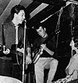 A youthful McCartney and Lennon perform in a low-ceilinged room with an audience member a few feet away.