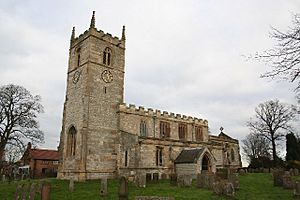 A stone church seen from the southwest.  On the left is the tower with a battlemented parapet and pinnacles, in the centre is the nave, also battlemented, and to the right  at a lower level is the chancel