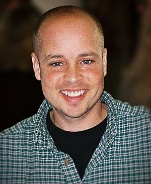 A portrait photograph of a man; he's wearing a checkered shirt while looking into the camera and smiling.