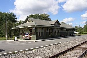 Image of a train depot that looks old but has been restored, with train tracks in the foreground.