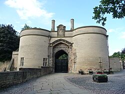 Low angle shot from the former moat now grassed over, looking up at twin stone towers with an arched bridge accessing the entrance to the right