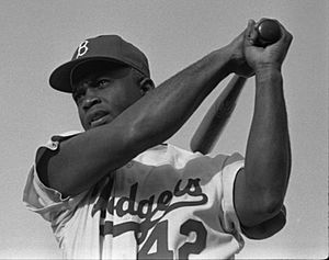 Waist-up portrait of black batter in his mid-thirties, in Brooklyn Dodgers uniform number 42, at end of swing with bat over left shoulder, looking at where a hit ball would be
