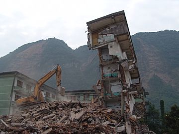 A collapsed structure being bulldozed, with a exposed mountain face in the background