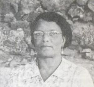 Black and white photograph of an African American woman with short hair and glasses in front of a rock wall.