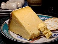 A wedge of yellow-white cheese, with a large crumbly piece broken off, served with a cracker