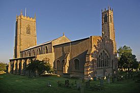 View of the church bathed in early morning sunlight.  There is a large tower at the further end, and a small tower beside the chancel.