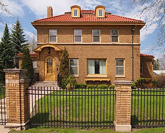 Two-story brick house with a Spanish tile roof, behind a wrought-iron fence