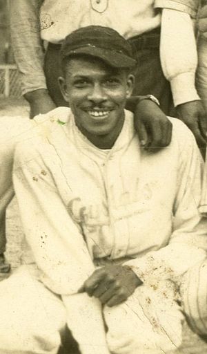 A man in a baseball uniform and cap smiling at the camera, part of a group photo